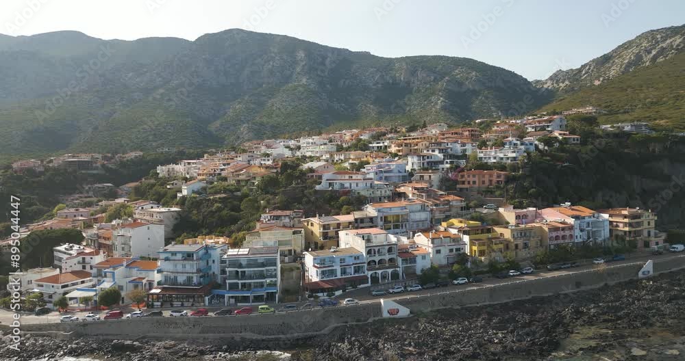 Seaside Townhouses In Cala Gonone Surrounded By Mountains In Sardinia, Italy. aerial shot Seaside Townhouses In Cala Gonone Surrounded By Mountains In Sardinia, Italy. aerial shot