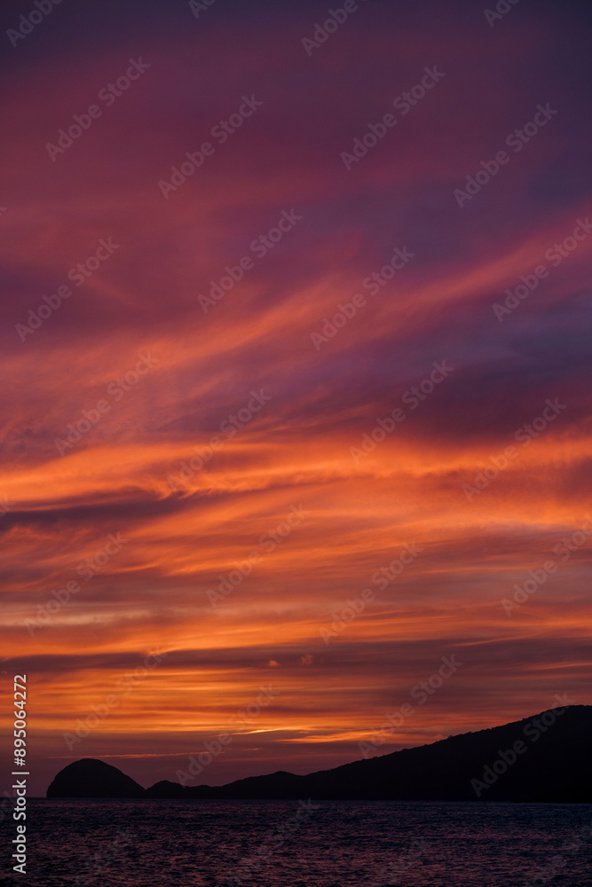 Last light of day under a dramatic glowing sky with a silhouetted landscape with clouds streaking the sky; Bai Nhat, Con Dao, Vietnam Last light of day under a dramatic glowing sky with a silhouetted landscape with clouds streaking the sky; Bai Nhat, Con Dao, Vietnam