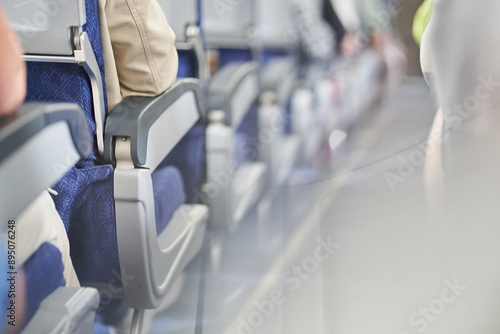 One side into the distance is a row of seats on an airplane. People are sitting with their backs to the camera in the passenger compartment along the aisle. With a place to copy. High quality photo