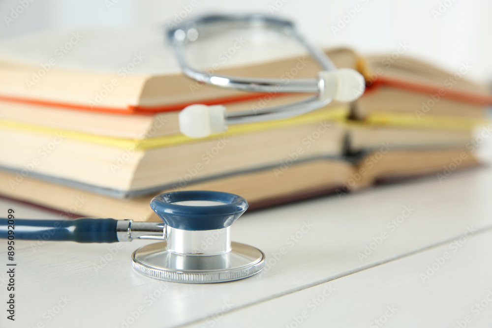 One new medical stethoscope and books on white wooden table, closeup One new medical stethoscope and books on white wooden table, closeup