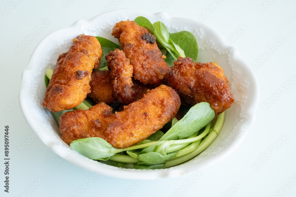 Fried chicken breast in bite-sized pieces with greens in a white bowl close-up Fried chicken breast in bite-sized pieces with greens in a white bowl close-up