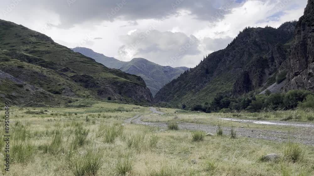 Mountain Valley Landscape. Lush Green Slopes, Rolling Hills, and a Tranquil Dirt Path Under a Dramatic Cloudy Sky