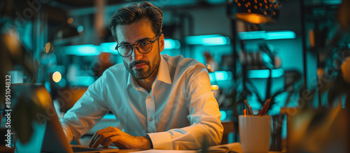 A man is sitting at a desk in an office, working on his computer. He's wearing glasses and a white shirt. Manager at work. Copy space.