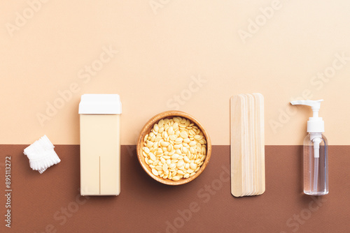 Depilatory background featuring various hair removal accessories: honey wax cartridge, granulated wax, body oil or lotion, shower cap, and wooden spatulas on beige-brown.