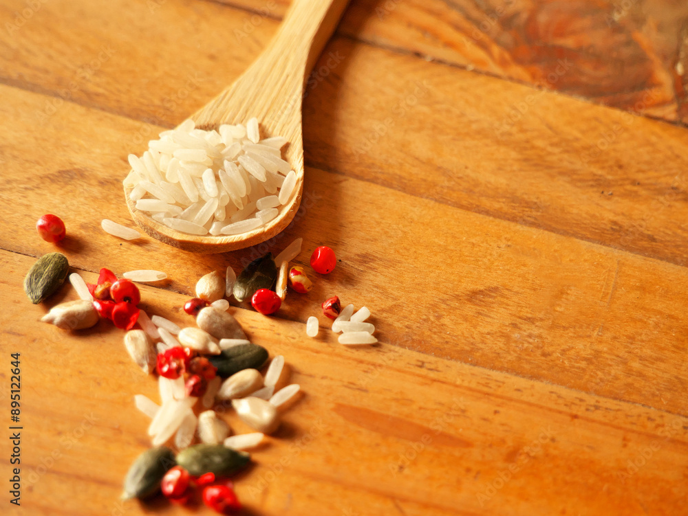Raw rice grains in a wooden spoon, and condiment seeds scattered on the side Raw rice grains in a wooden spoon, and condiment seeds scattered on the side