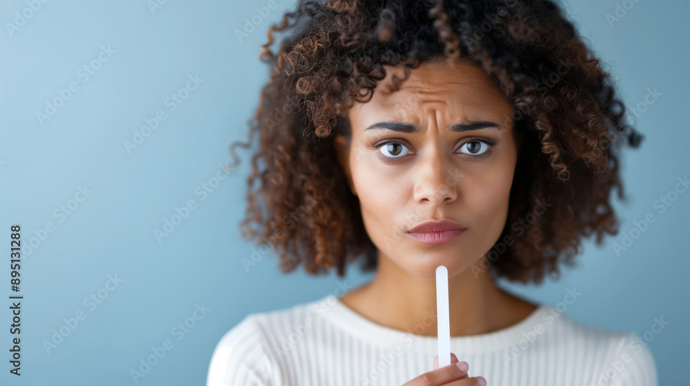 Fototapeta premium A woman looking at a positive pregnancy test with a conflicted expression, neutral background 