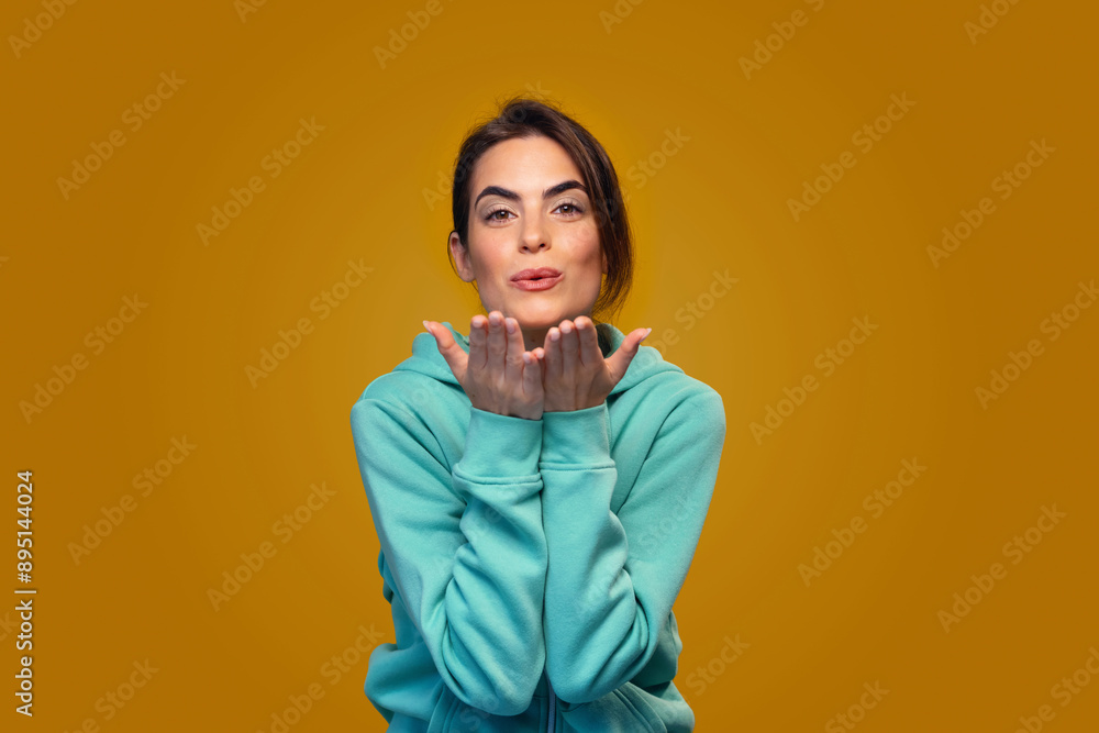 Cute woman with blue sweater sending a kiss while posing in front of camera on isolated orange Cute woman with blue sweater sending a kiss while posing in front of camera on isolated orange