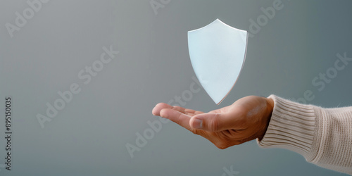 Hand holding a shield  on a grey background with copy space

 photo