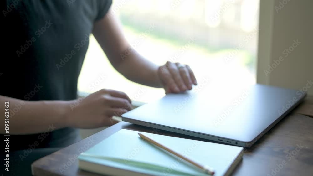 A woman opens her laptop at a home desk, with a notebook and pencil nearby, preparing to work or study. High quality 4k footage A woman opens her laptop at a home desk, with a notebook and pencil nearby, preparing to work or study. High quality 4k footage