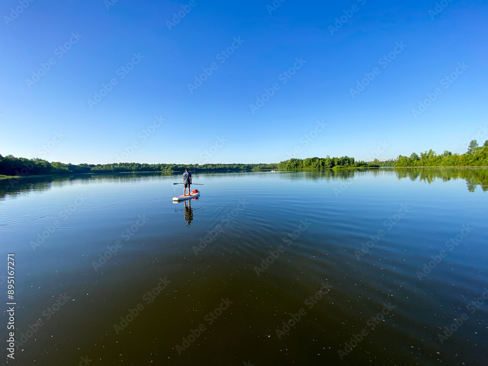 A serene scene unfolds as a person peacefully paddles on a tranquil lake, surrounded by natures beauty under a clear sky, creating a calm and peaceful atmosphere in this tranquil setting A serene scene unfolds as a person peacefully paddles on a tranquil lake, surrounded by natures beauty under a clear sky, creating a calm and peaceful atmosphere in this tranquil setting
