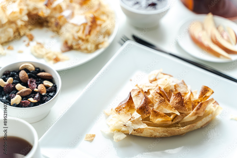 Apple dessert, fila pastry pie on a square white plate with a cup of tea and nuts on a light background. Apple dessert, fila pastry pie on a square white plate with a cup of tea and nuts on a light background.