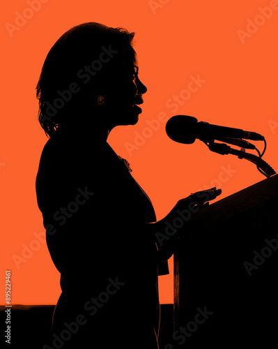 side view semi-silhouette profile of an African American woman speaking at a podium, red background photo