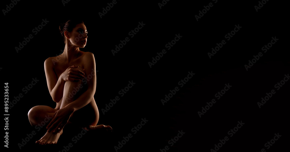 A woman sits alone in a dark room, her arms crossed and her legs crossed. The only light is from the side, illuminating her profile and creating a sense of mystery, copy space