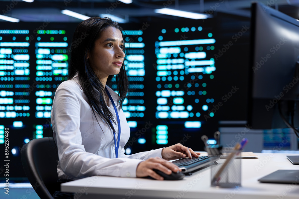 Fototapeta premium Indian woman doing yearly checkup to prolong data center electronics life span and avoid downtime. IT employee in server room monitoring server infrastructure components using PC