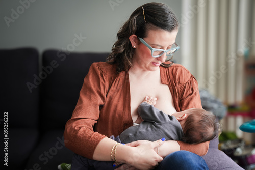 Young mother breastfeeding her baby, the woman is sitting on a sofa and looking and her baby