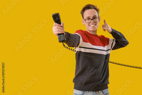 Cool young man with receiver showing "call me" gesture on yellow background