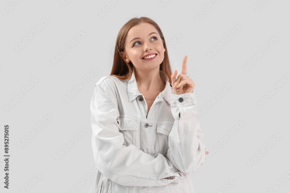 Pretty young woman in stylish clothes pointing at something on light background Pretty young woman in stylish clothes pointing at something on light background