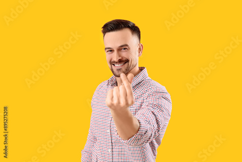 Handsome man making heart with his fingers on yellow background