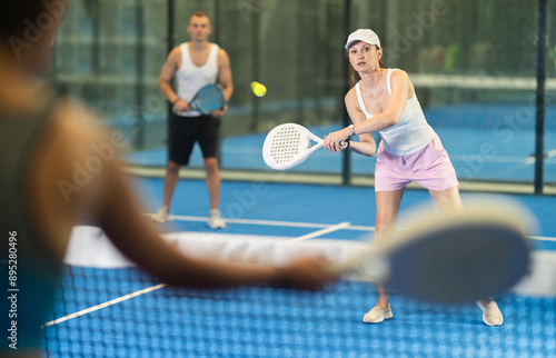 Adult woman and young man in doubles play against young woman on tennis court photo