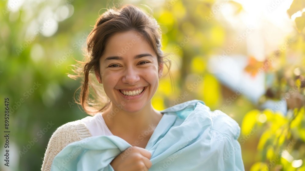 Woman smiling outdoors on sunny day holding a light blue shirt. Woman smiling outdoors on sunny day holding a light blue shirt.