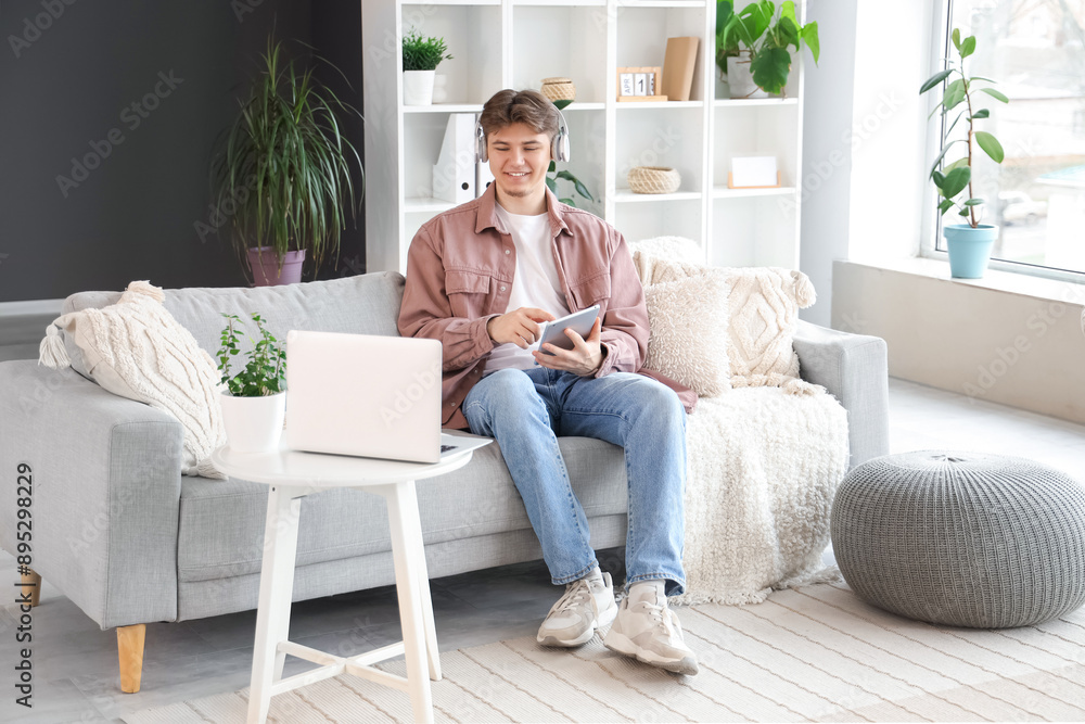 Male student in headphones with tablet computer studying online on sofa at home Male student in headphones with tablet computer studying online on sofa at home