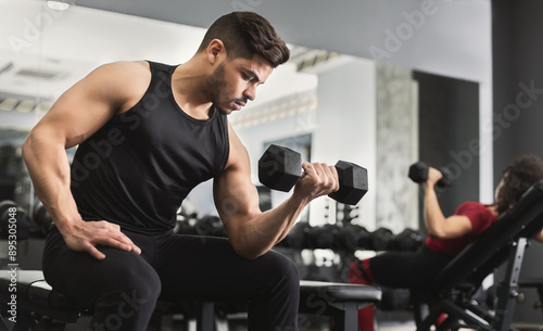 Arab muscular man doing biceps workouts with dumbbells in gym, copy space photo