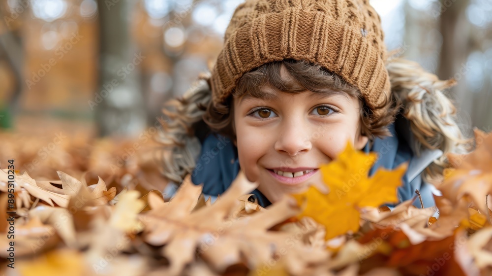 Fototapeta premium A young child smiling warmly while surrounded by autumn leaves, dressed in cozy, warm clothing and a knitted hat, epitomizing the essence of a joyful autumn day.