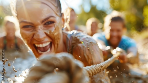 Group of individuals engaging in a spirited tug-of-war game in muddy conditions, showcasing teamwork, determination, and enjoyment amidst an outdoor setting. photo