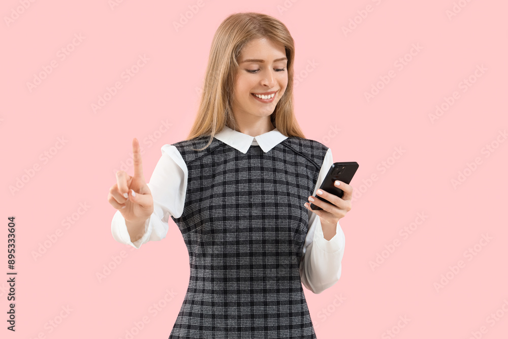 Fototapeta premium Young businesswoman with mobile phone using virtual screen on pink background