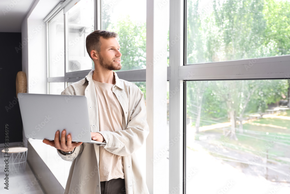 Handsome man using laptop near window at home
