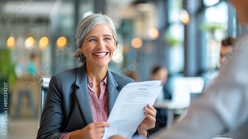 Fototapeta Naklejka Na Ścianę i Meble -  Smiling mature business woman hr holding cv document at job interview. Happy mid aged professional banking manager or lawyer consulting client sitting at workplace in corporate office meeting.