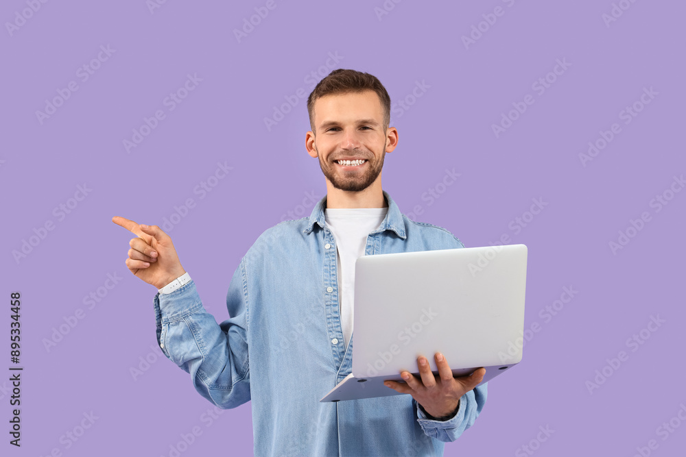 Handsome man with laptop pointing at something on lilac background Handsome man with laptop pointing at something on lilac background