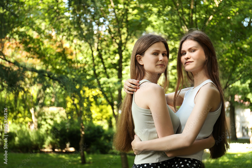 Portrait of two beautiful twin sisters in park, space for text Portrait of two beautiful twin sisters in park, space for text