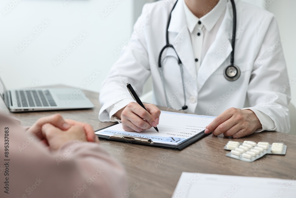 Doctor writing prescription for patient at wooden table in clinic, closeup Doctor writing prescription for patient at wooden table in clinic, closeup