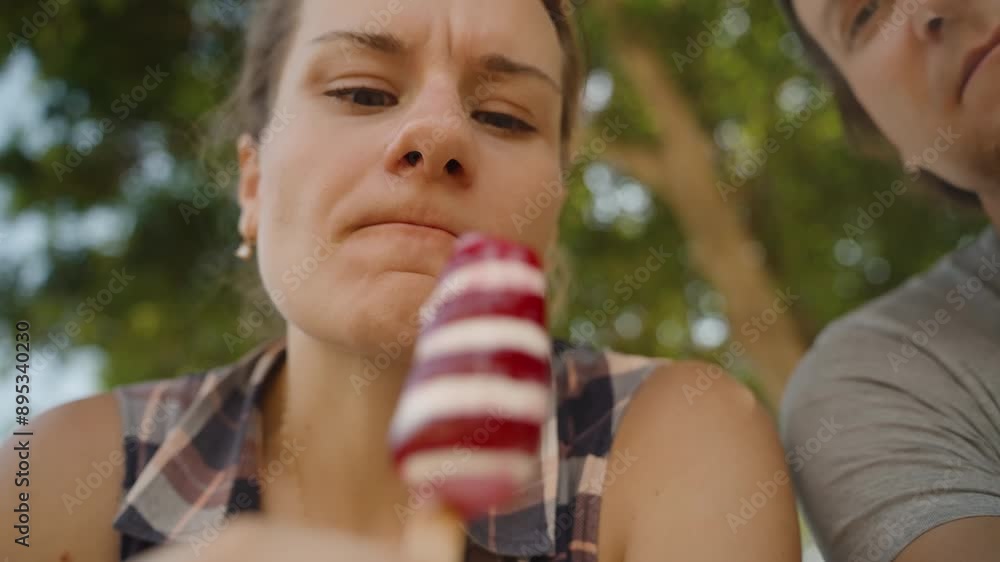 Woman Shares a Striped Popsicle with Her Boyfriend, Enjoying a Sweet Moment Together. Woman Shares a Striped Popsicle with Her Boyfriend, Enjoying a Sweet Moment Together.