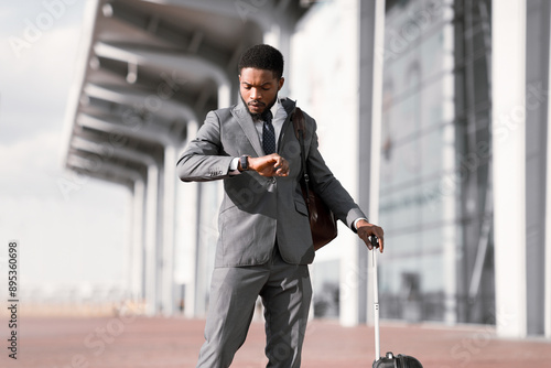 Business Traveler Checking Time On his Wristwatch At Airport, Walking Outdoors photo