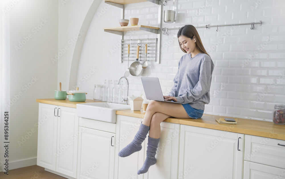 Portrait beautiful asian creative woman relax sit on kitchen counter use computer laptop. Smile happy asian girl drink coffee at table home. Freelance small business asian owner sme work from home Portrait beautiful asian creative woman relax sit on kitchen counter use computer laptop. Smile happy asian girl drink coffee at table home. Freelance small business asian owner sme work from home