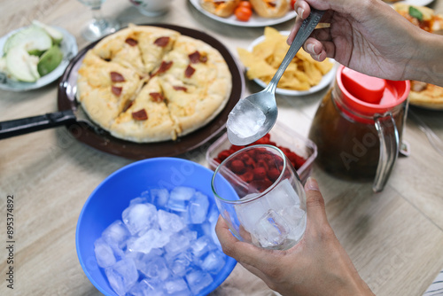 Hand Putting Ice Into Glass Cup With Spoon And Various Foods On The Table For Dining Party