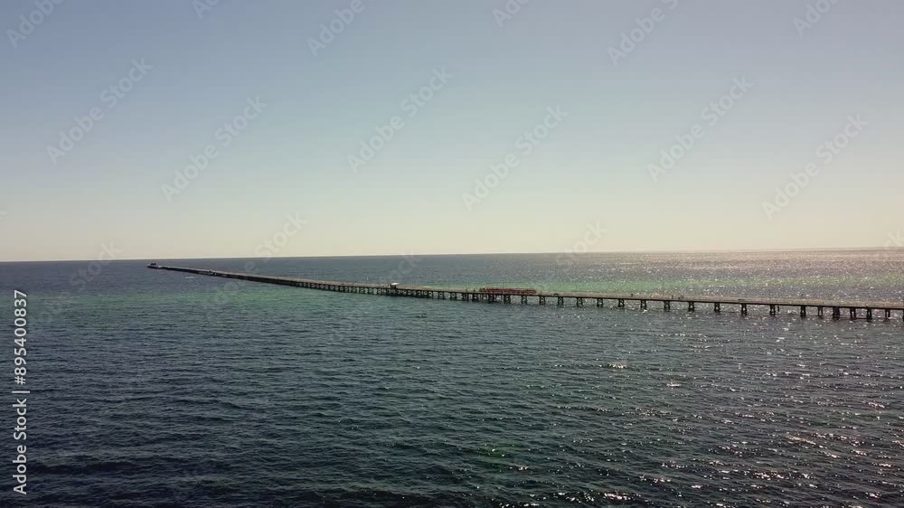 Wide view of Busselton Jetty in silhouette with tourist train heading out along pier Wide view of Busselton Jetty in silhouette with tourist train heading out along pier