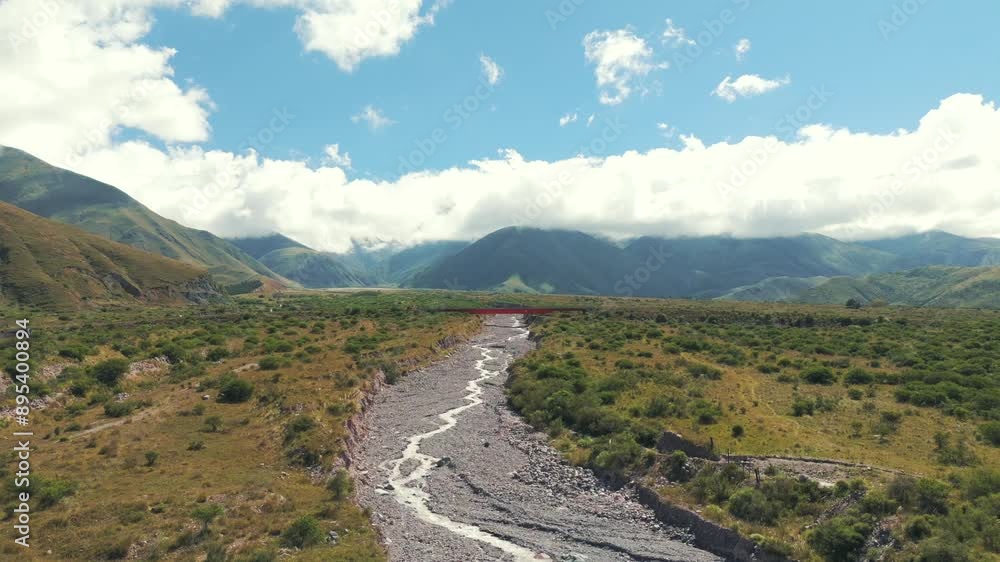 Panoramic view showing a nearly dry rocky river and a red bridge over Route 9 in the background, in Jujuy, Argentina. Panoramic view showing a nearly dry rocky river and a red bridge over Route 9 in the background, in Jujuy, Argentina.