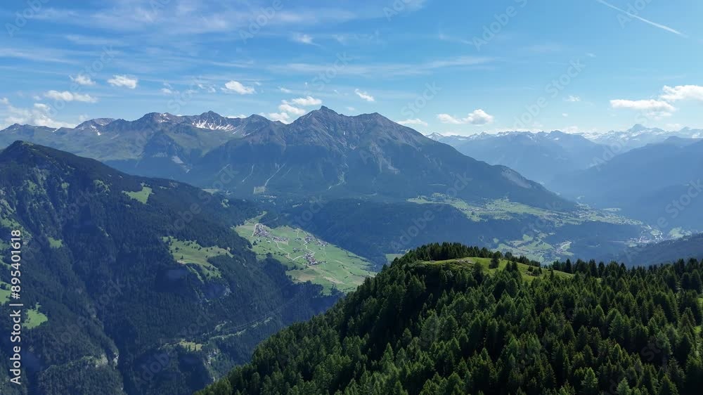 Aerial view of Muttner Höhe Mountains with idyllic trees and alps Panorama in Background. Sunny day with blue sky in Switzerland. Green mountains and scenic villages in the valley. Aerial view of Muttner Höhe Mountains with idyllic trees and alps Panorama in Background. Sunny day with blue sky in Switzerland. Green mountains and scenic villages in the valley.