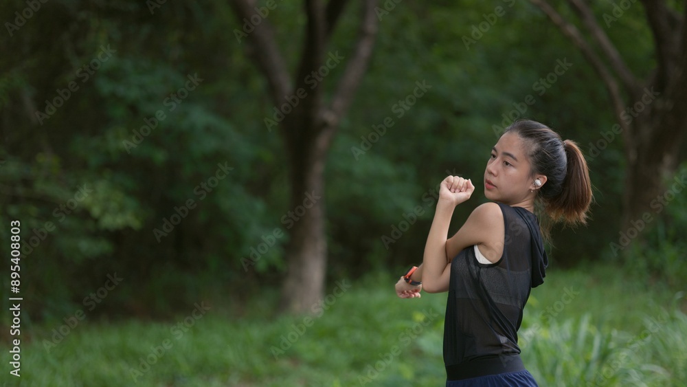 A woman is standing in a park, stretching her arms A woman is standing in a park, stretching her arms