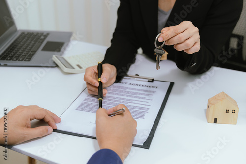 A real estate agent presents a property sale contract to a client. They discuss mortgage options, insurance, and the financial details of the investment. With the agreement signed, the keys to the new photo