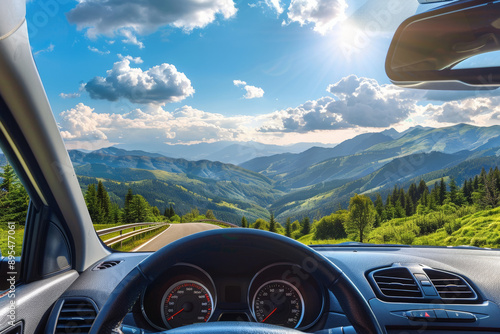 Front view of the inside car, driving on an asphalt road in summer through green forests and mountains with snow-capped peaks in sunny weather. The interior is visible from behind the steering wheel.  photo