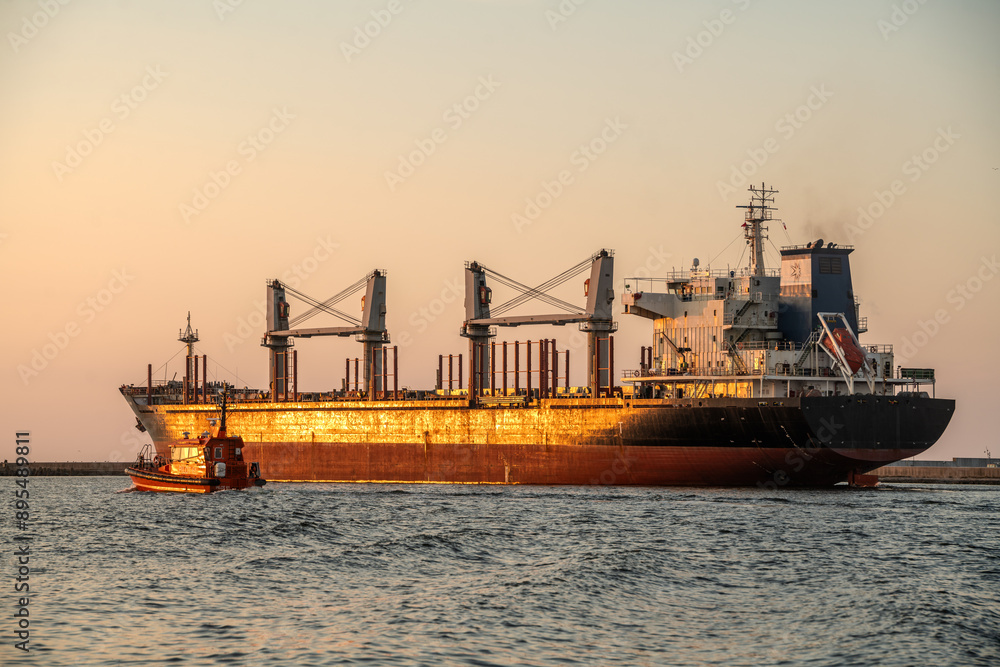 Fototapeta premium Bulk cargo vessel guided by a tugboat in the fairway to the port