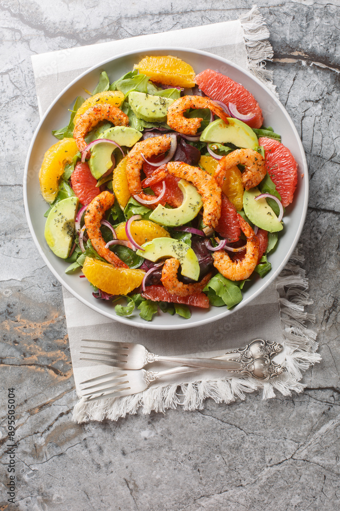 Fresh Cajun shrimp salad with oranges, avocado, grapefruit and leafy greens close-up in a plate on the table. Vertical top view from above