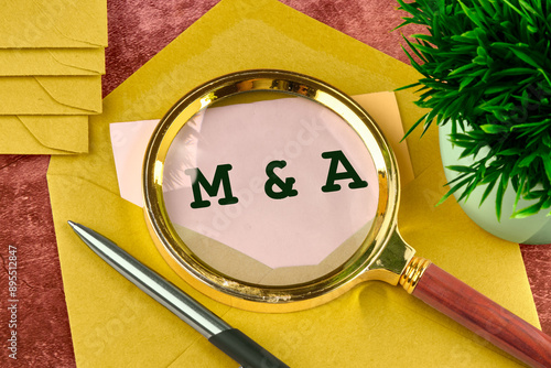 M and A Mergers and Acquisitions word concept. M and A through a magnifying glass in a letter peeking out of an envelope photo