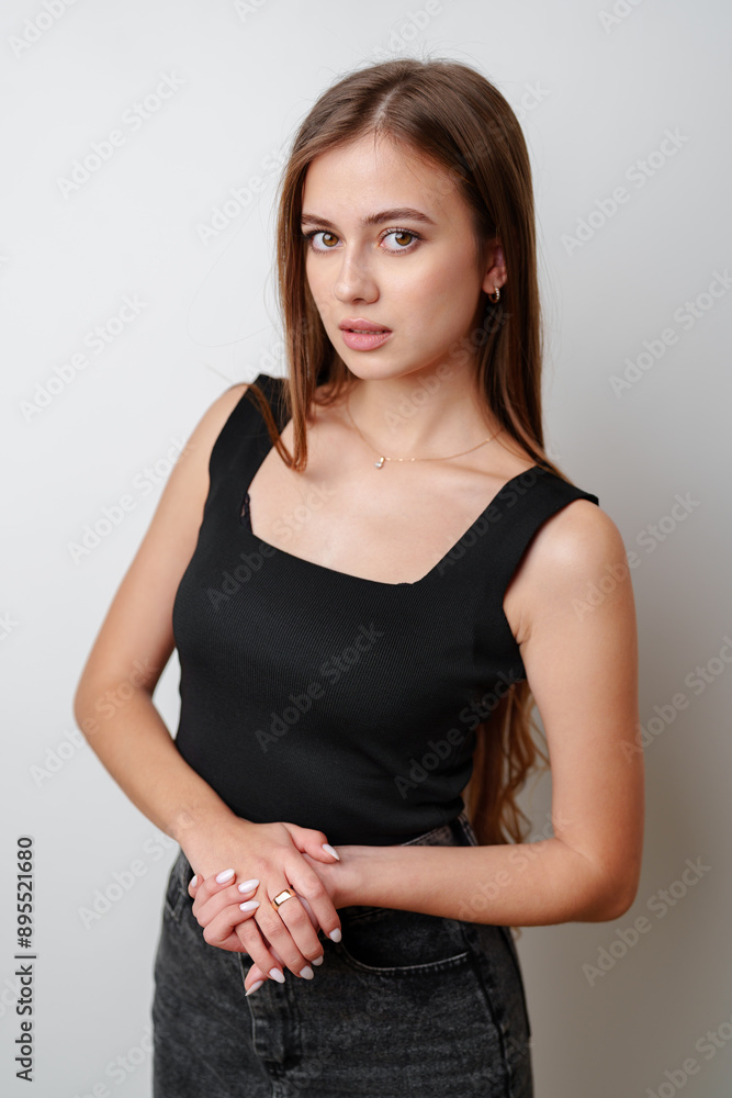 Young Woman Wearing Black Tank Top and Jeans Posing Against White Background Young Woman Wearing Black Tank Top and Jeans Posing Against White Background