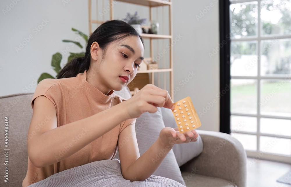 Young Woman Holding Birth Control Pill Pack While Sitting on a Sofa in a Modern Living Room Young Woman Holding Birth Control Pill Pack While Sitting on a Sofa in a Modern Living Room