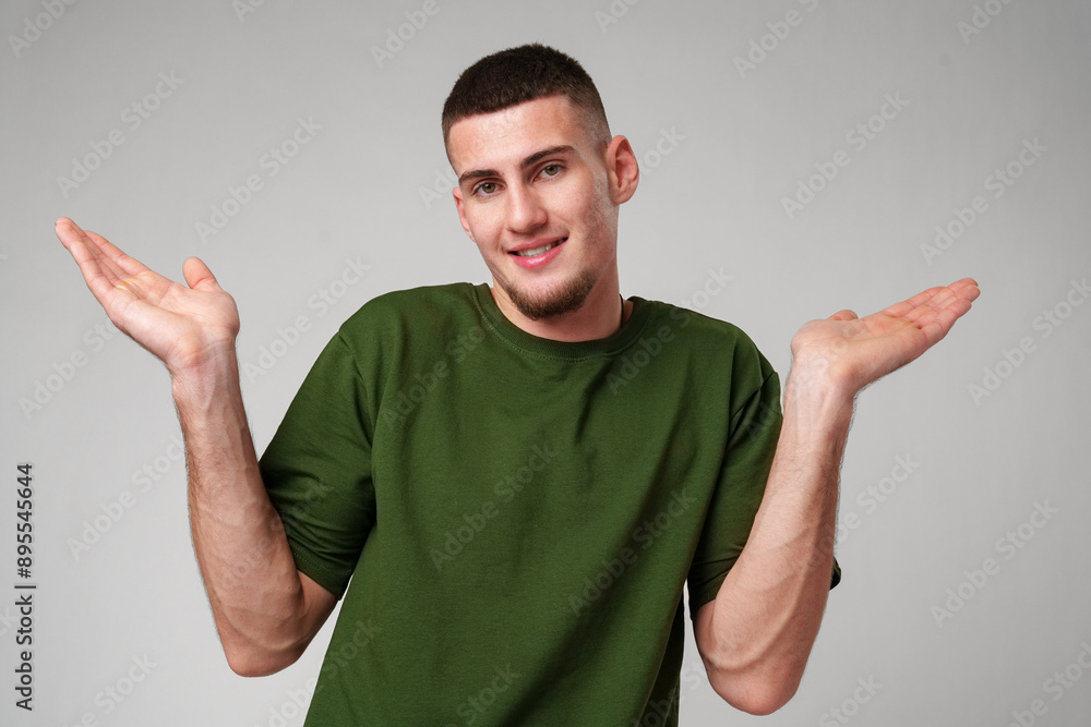 Fototapeta premium Young Man Wearing Green T-Shirt Gesturing With Both Hands in Front of a Plain White Background